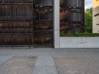 a sidewalk with a bike leans against a wall, in front of a building with two barrels