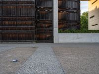 a sidewalk with a bike leans against a wall, in front of a building with two barrels