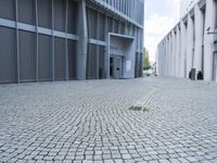 an empty street in front of a concrete building with doors open and people walking by