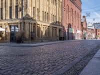 a cobblestone street in front of a yellow brick building in the city with many windows