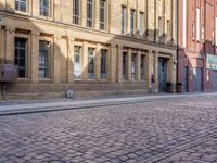 a cobblestone street in front of a yellow brick building in the city with many windows