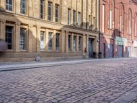 a cobblestone street in front of a yellow brick building in the city with many windows