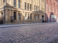 a cobblestone street in front of a yellow brick building in the city with many windows