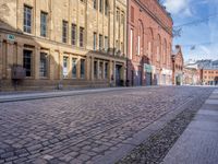 a cobblestone street in front of a yellow brick building in the city with many windows