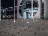 the outside of a large building lit up at night with white lights and circles in the courtyard