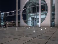 the outside of a large building lit up at night with white lights and circles in the courtyard