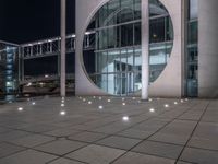 the outside of a large building lit up at night with white lights and circles in the courtyard