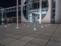 the outside of a large building lit up at night with white lights and circles in the courtyard