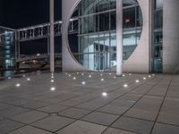 the outside of a large building lit up at night with white lights and circles in the courtyard