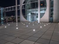 the outside of a large building lit up at night with white lights and circles in the courtyard