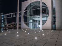 the outside of a large building lit up at night with white lights and circles in the courtyard