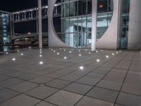 the outside of a large building lit up at night with white lights and circles in the courtyard