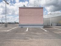 a parking lot with pink building and sky in background that includes several tall white buildings