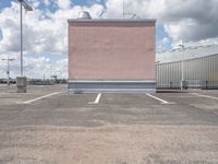 a parking lot with pink building and sky in background that includes several tall white buildings