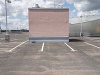 a parking lot with pink building and sky in background that includes several tall white buildings