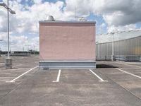 a parking lot with pink building and sky in background that includes several tall white buildings