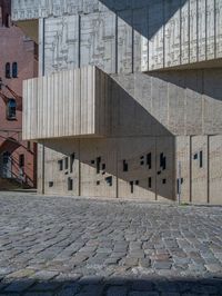 cobblestone driveway surrounded by modern buildings on sunny day with sun reflecting onto the windows