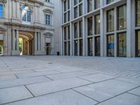 an empty brick courtyard area with two stone columns and two arched windows in the background