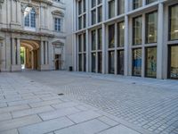 an empty brick courtyard area with two stone columns and two arched windows in the background