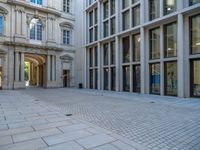 an empty brick courtyard area with two stone columns and two arched windows in the background