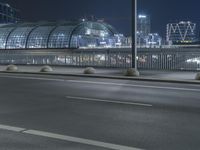 the empty city road is empty by the tall building in the background at night with light streaking on the buildings