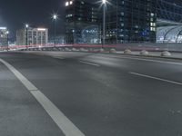 the empty city road is empty by the tall building in the background at night with light streaking on the buildings