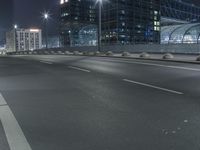 the empty city road is empty by the tall building in the background at night with light streaking on the buildings