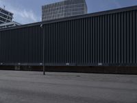 an empty parking lot with a large black fence in the background and tall buildings on both sides