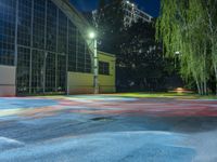 the basketball court is brightly colored and empty at night in a urban park in the evening