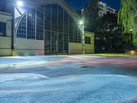 the basketball court is brightly colored and empty at night in a urban park in the evening