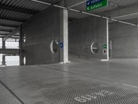 an empty concrete garage with signs on the ceiling and exit doors that lead out to an empty area