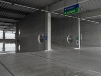 an empty concrete garage with signs on the ceiling and exit doors that lead out to an empty area