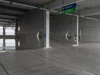 an empty concrete garage with signs on the ceiling and exit doors that lead out to an empty area