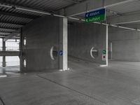 an empty concrete garage with signs on the ceiling and exit doors that lead out to an empty area