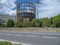 there is an empty street in front of a huge building under construction with trees around