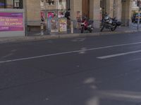 an empty road with two motorcycles parked outside the building in the background and people walking around