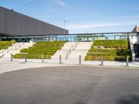 the stairs lead to a large building in front of a green sloped hillside and two parking spaces