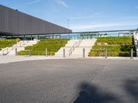 the stairs lead to a large building in front of a green sloped hillside and two parking spaces