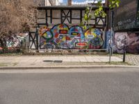 a street with various graffiti and a painted wall in the background on a corner of it