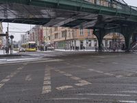 a train traveling under a bridge over a street filled with traffic on a snowy day