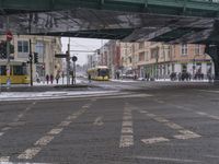 a train traveling under a bridge over a street filled with traffic on a snowy day