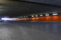 a large brick sidewalk with a red wall in it's center and lights shining on the sides of a street