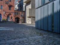 cobblestone driveway surrounded by modern buildings on sunny day with sun reflecting onto the windows