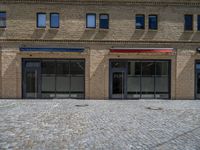 the sidewalk is paved with stones and has a bench in front of it, with no people inside