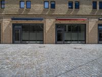 the sidewalk is paved with stones and has a bench in front of it, with no people inside