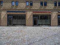 the sidewalk is paved with stones and has a bench in front of it, with no people inside