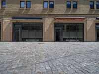 the sidewalk is paved with stones and has a bench in front of it, with no people inside