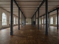 a wide room with columns and windows, all covered in wooden planks and steel poles