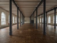 a wide room with columns and windows, all covered in wooden planks and steel poles