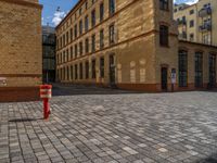 a sidewalk with chairs next to the brick building on the side, some have stairs and some buildings in the background